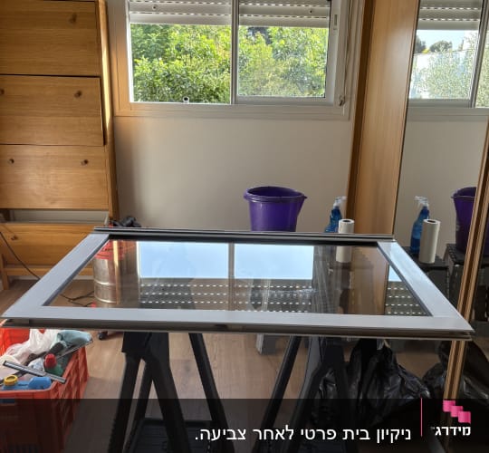 חדר עם חלון, דלי סגול, בקבוקי ניקוי ושולחן עבודה